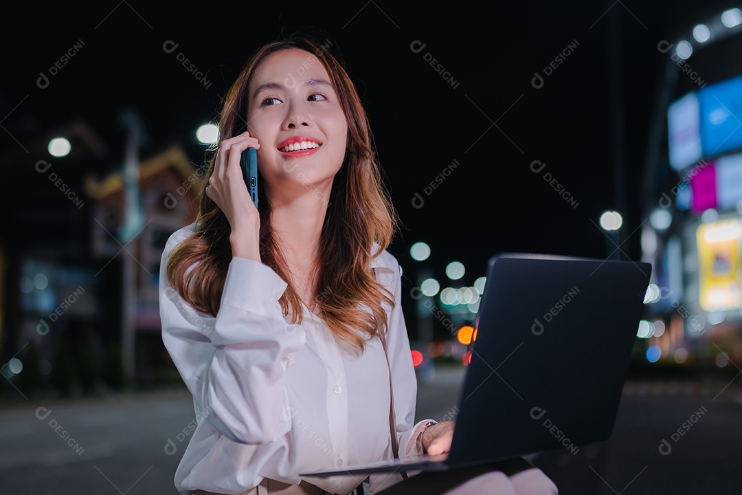 Encantadora empresária asiática usa laptop na cidade à noite