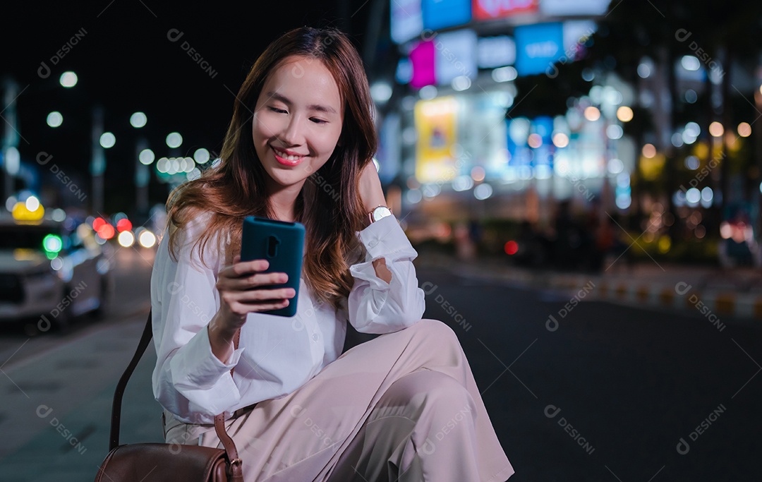 Encantadora empresária asiática usa telefone celular na cidade à noite