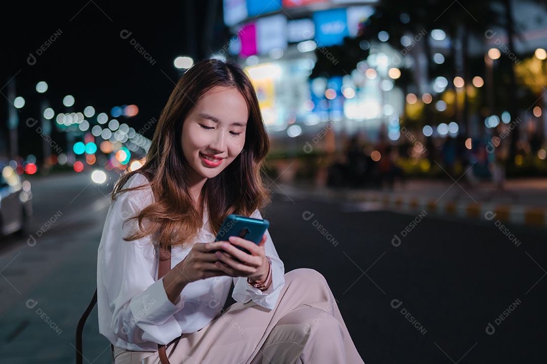 Encantadora empresária asiática usa telefone celular na cidade à noite