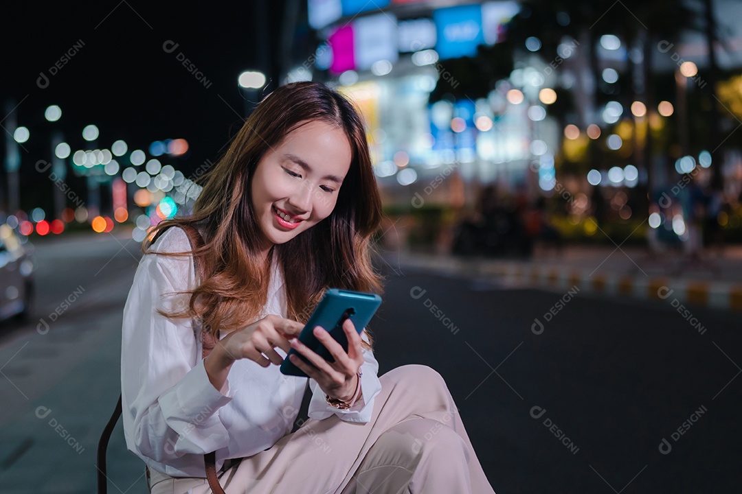 Encantadora empresária asiática usa telefone celular na cidade à noite