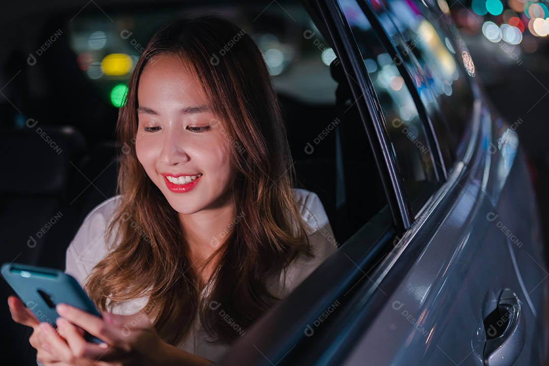 Sorrindo da empresária asiática bem-sucedida, use o smartphone móvel sentado no banco de trás do carro
