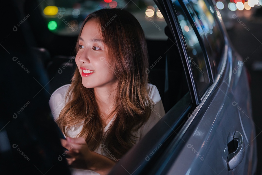 Sorrindo da empresária asiática bem-sucedida, use o smartphone móvel sentado no banco de trás do carro