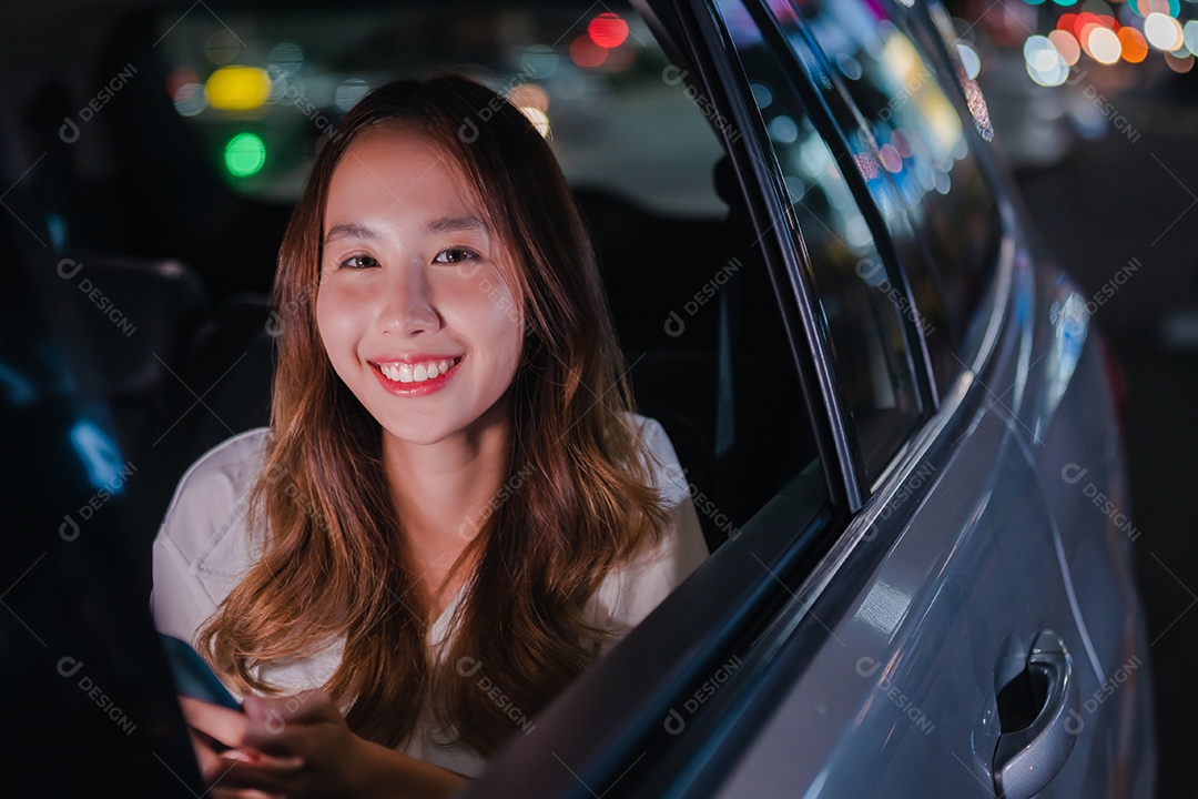 Sorrindo da empresária asiática bem-sucedida, use o smartphone móvel sentado no banco de trás do carro