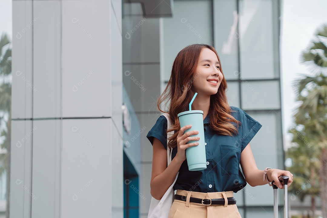 Empresária asiática sorridente segura mala de viagem  e copo ecológico reutilizável