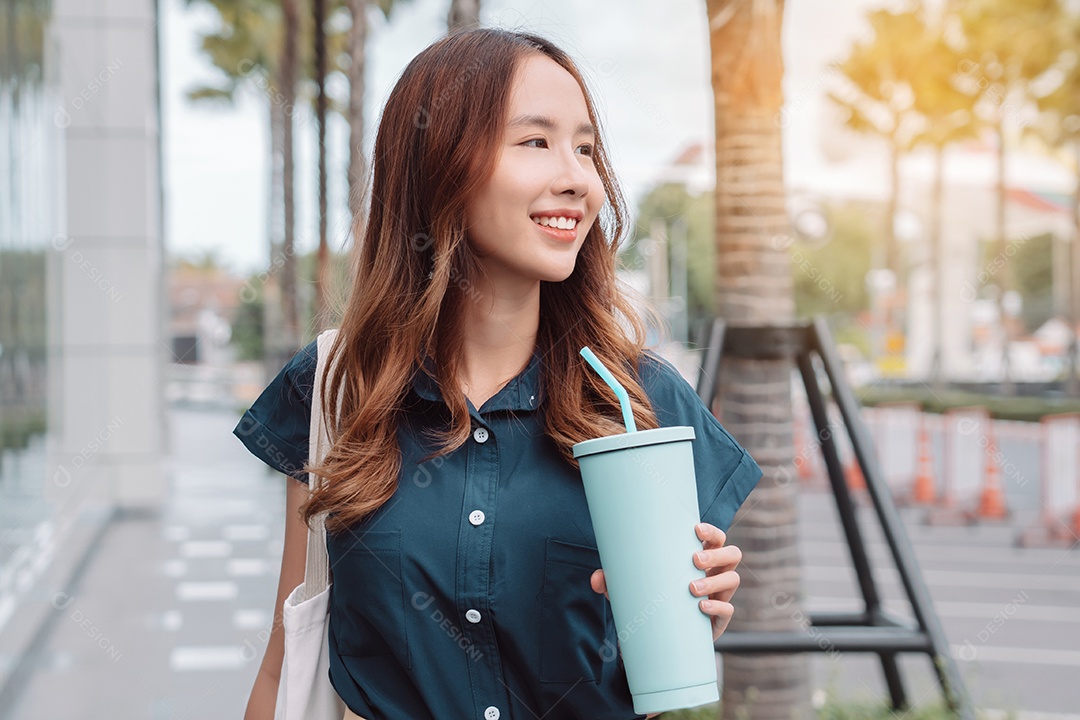 Empresária asiática sorridente segura mala de viagem  e copo ecológico reutilizável