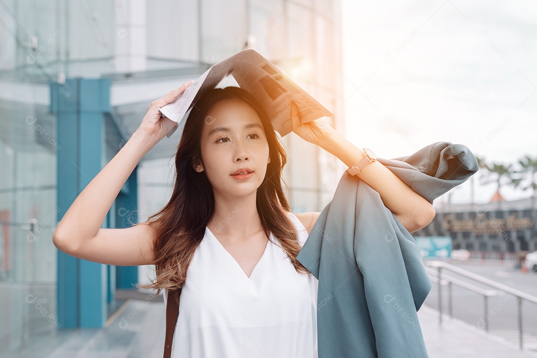 A emoção de estresse da mulher asiática pega o jornal cobre o rosto do sol na cidade moderna