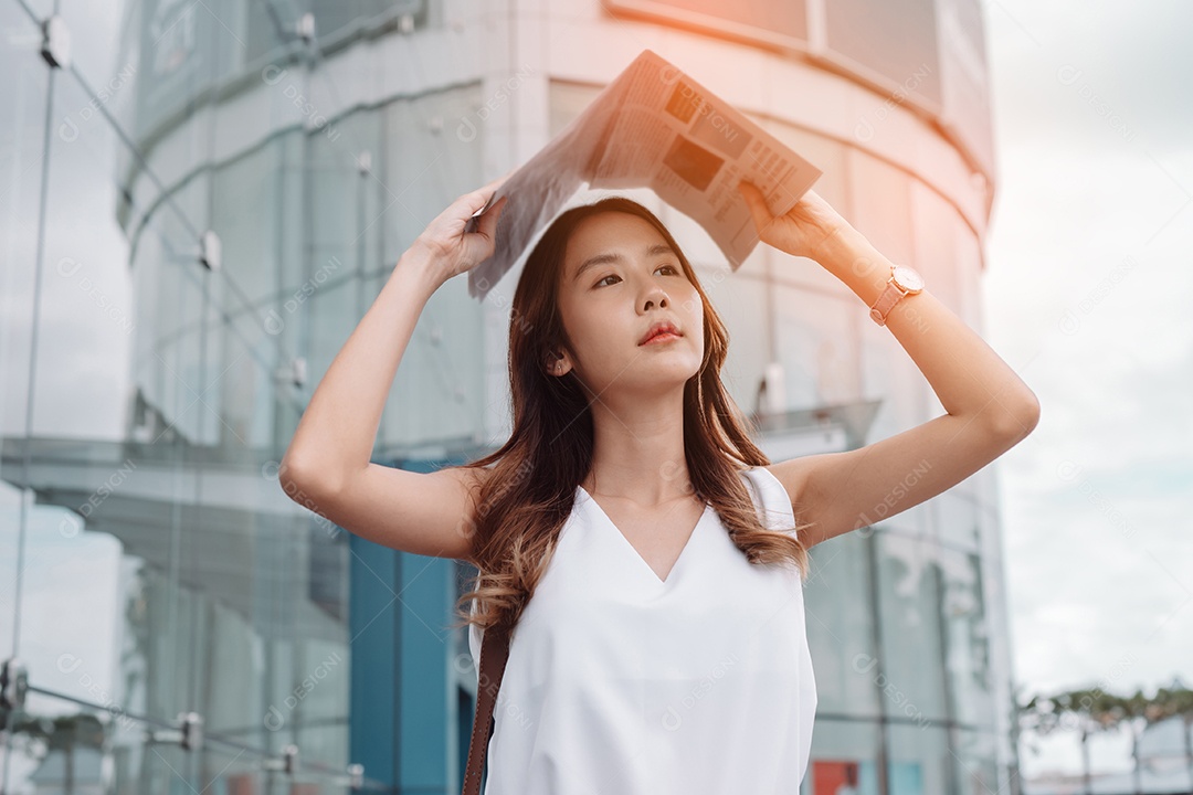 A emoção de estresse da mulher asiática pega o jornal cobre o rosto do sol na cidade moderna