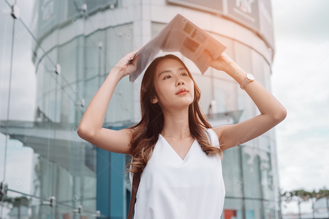 A emoção de estresse da mulher asiática pega o jornal cobre o rosto do sol na cidade moderna