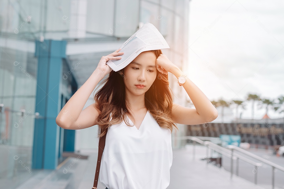 A emoção de estresse da mulher asiática pega o jornal cobre o rosto do sol na cidade moderna
