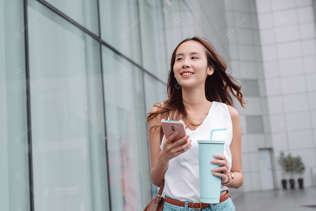 Empresária asiática sorridente usa smartphone e segura copo ecológico reutilizável