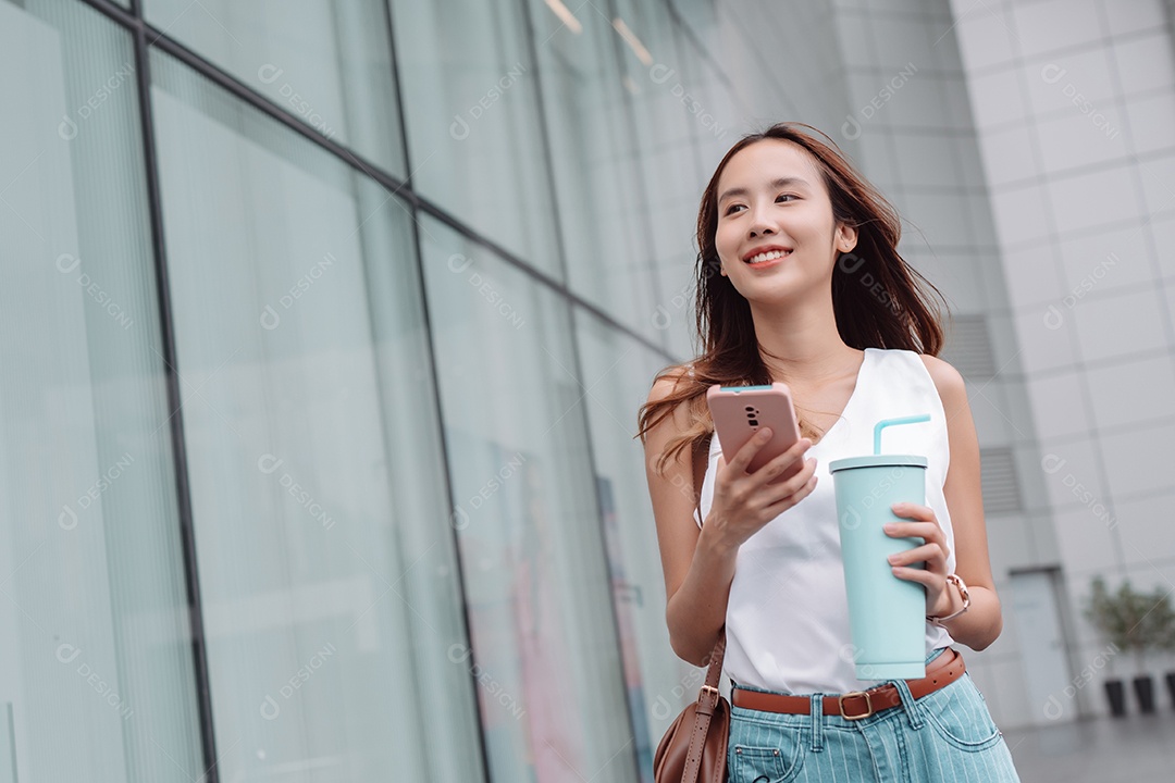 Empresária asiática sorridente usa smartphone e segura copo ecológico reutilizável