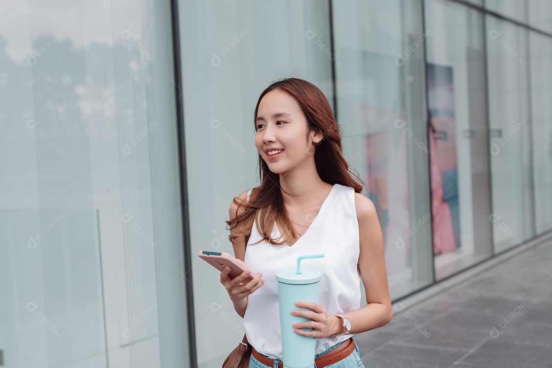 Empresária asiática sorridente usa smartphone e segura copo ecológico reutilizável