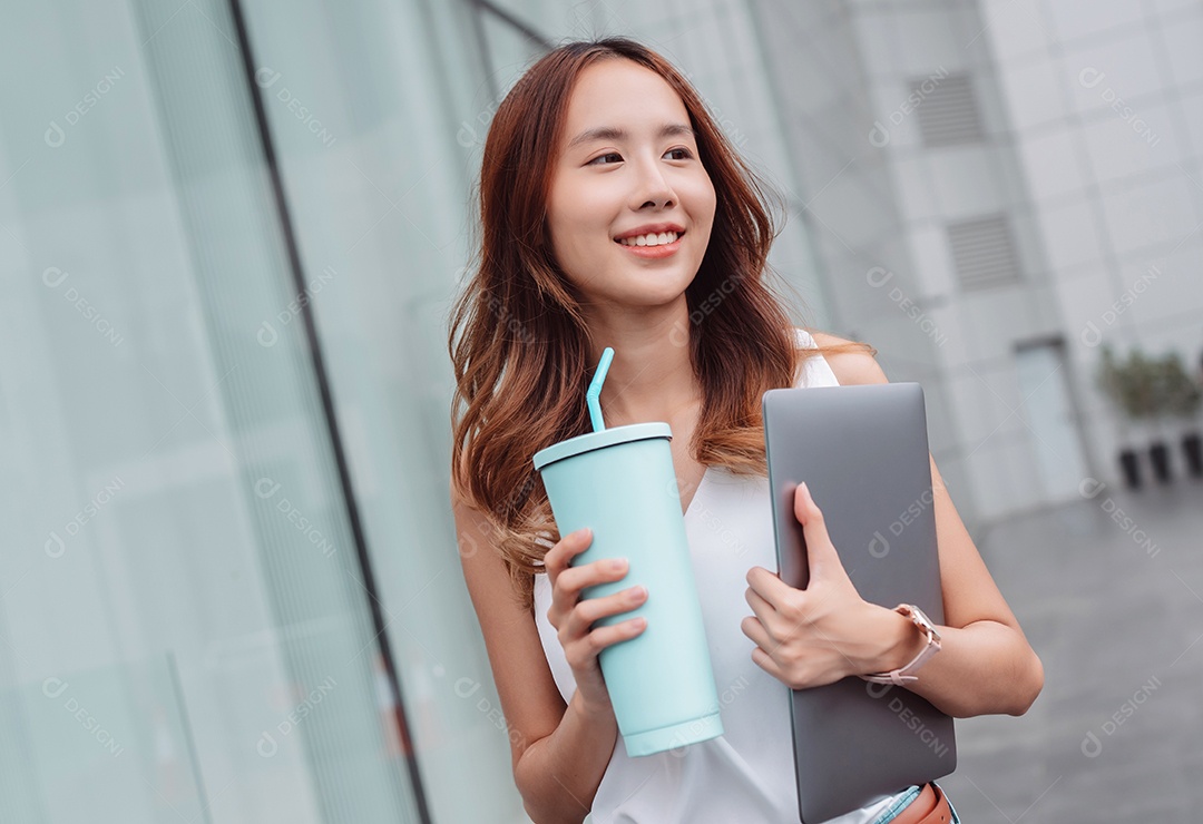 Empresária asiática sorridente segura um copo ecológico reutilizável e um laptop