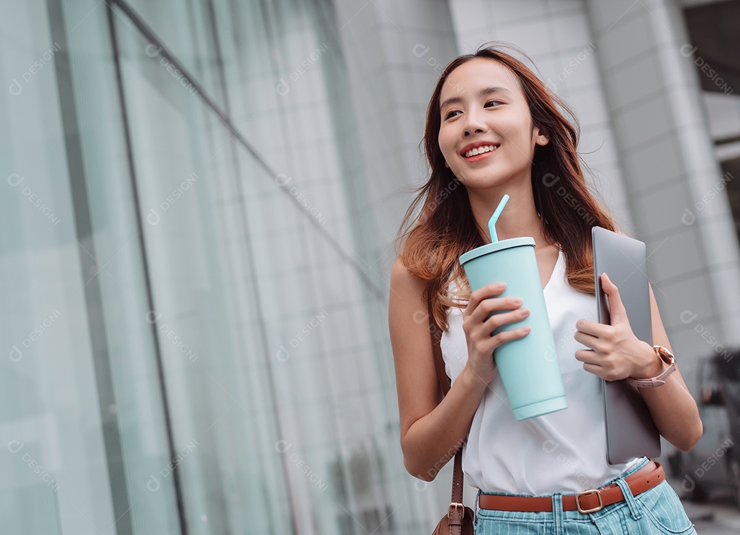 Empresária asiática sorridente segura um copo ecológico reutilizável e um laptop