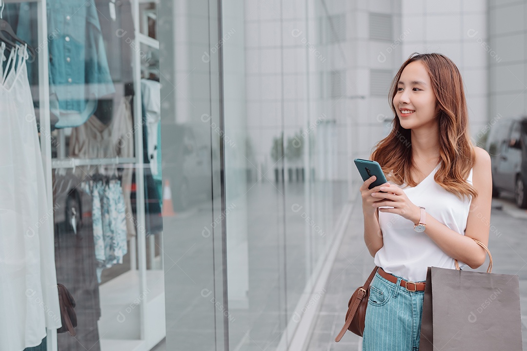 Linda mulher asiática usa smartphone e segura uma sacola de compras