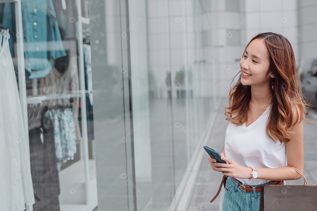 Linda mulher asiática usa smartphone e segura uma sacola de compras