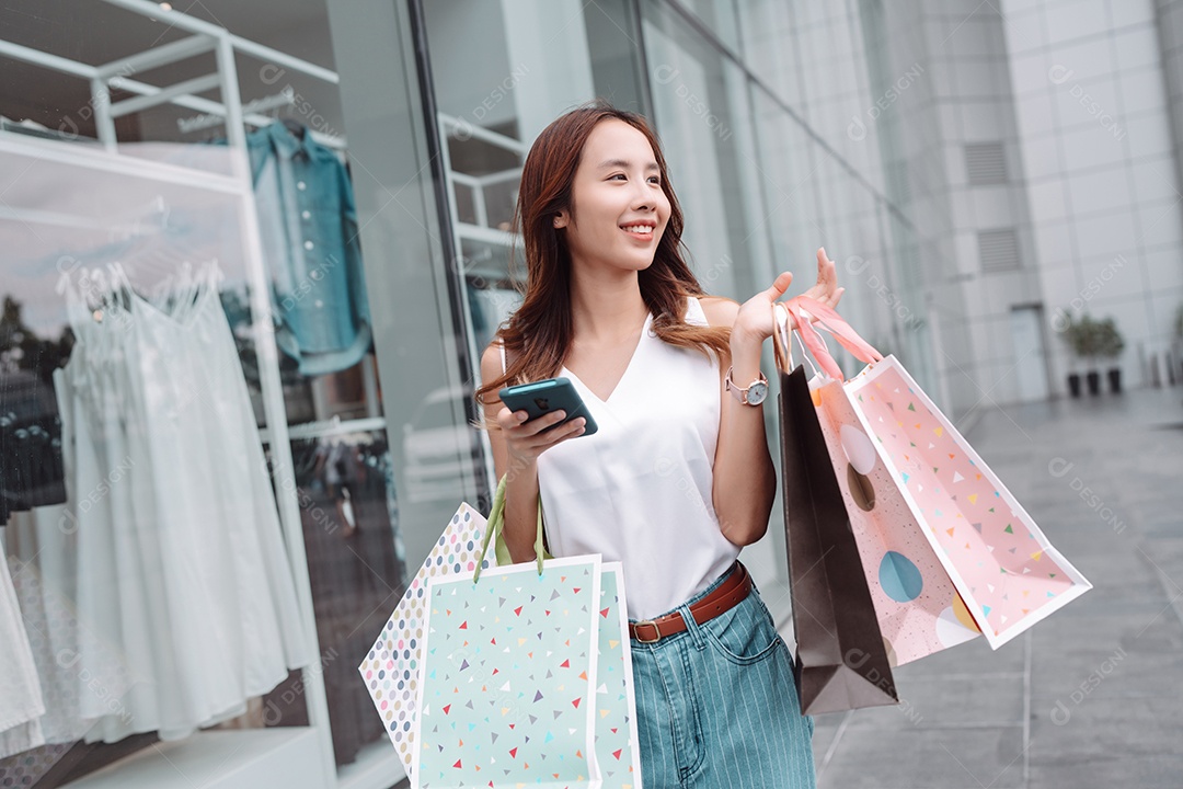 Linda mulher asiática usa smartphone e segura sacolas de compras