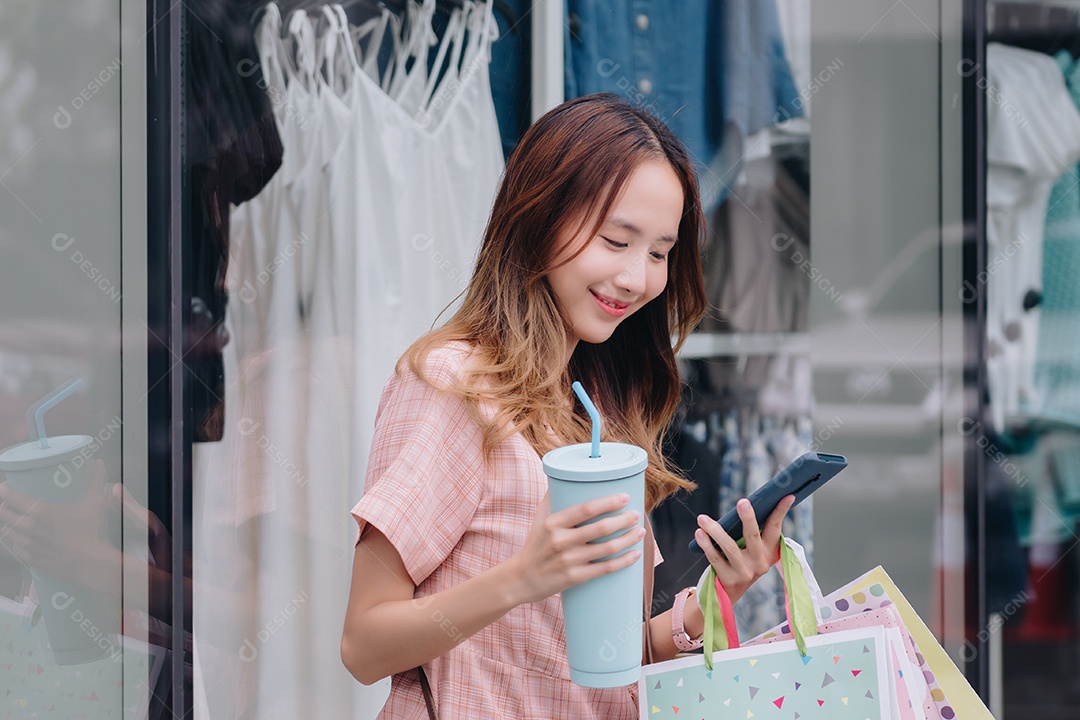 Compradora cliente mulher asiática usando smartphone e segurando copo ecológico reutilizável no shopping