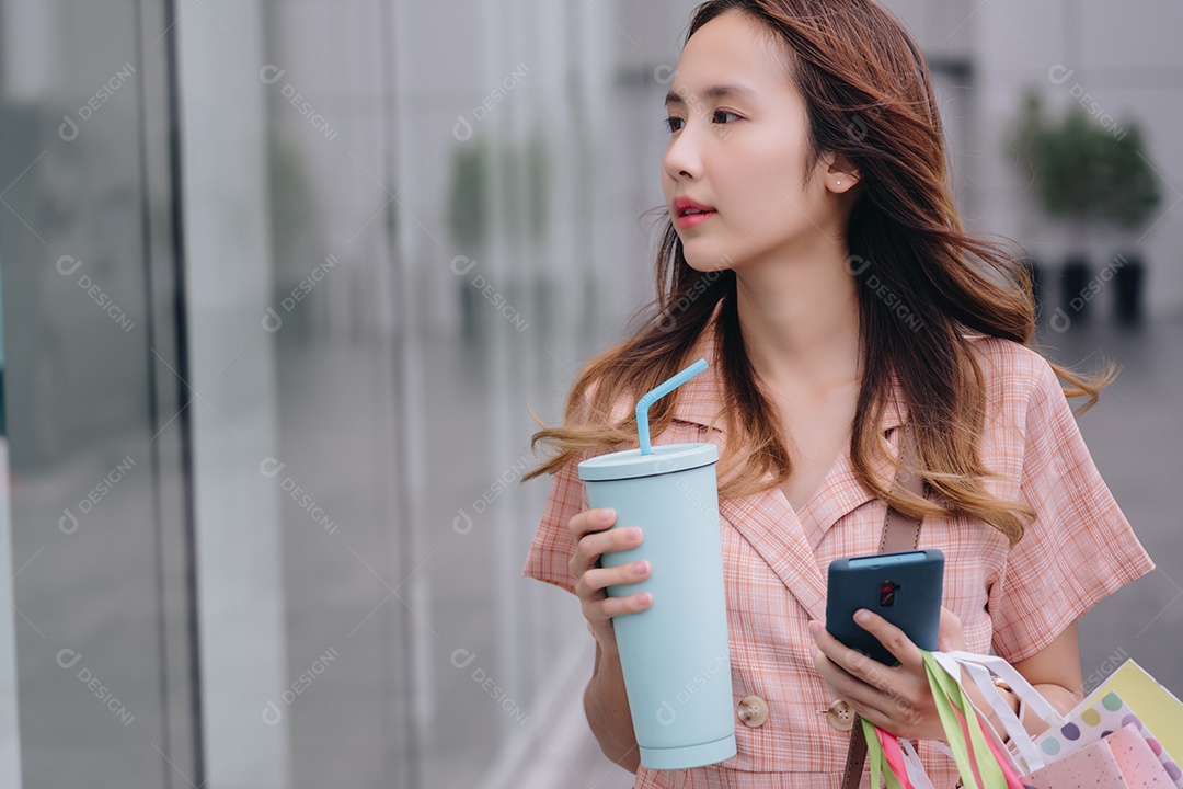 Compradora cliente mulher asiática usando smartphone e segurando copo ecológico reutilizável no shopping