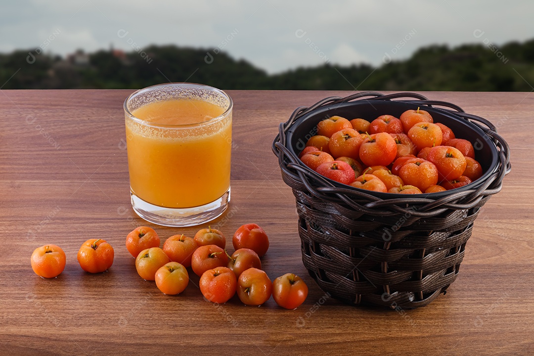 Suco de acerola e acerolas cruas na mesa de madeira na natureza.