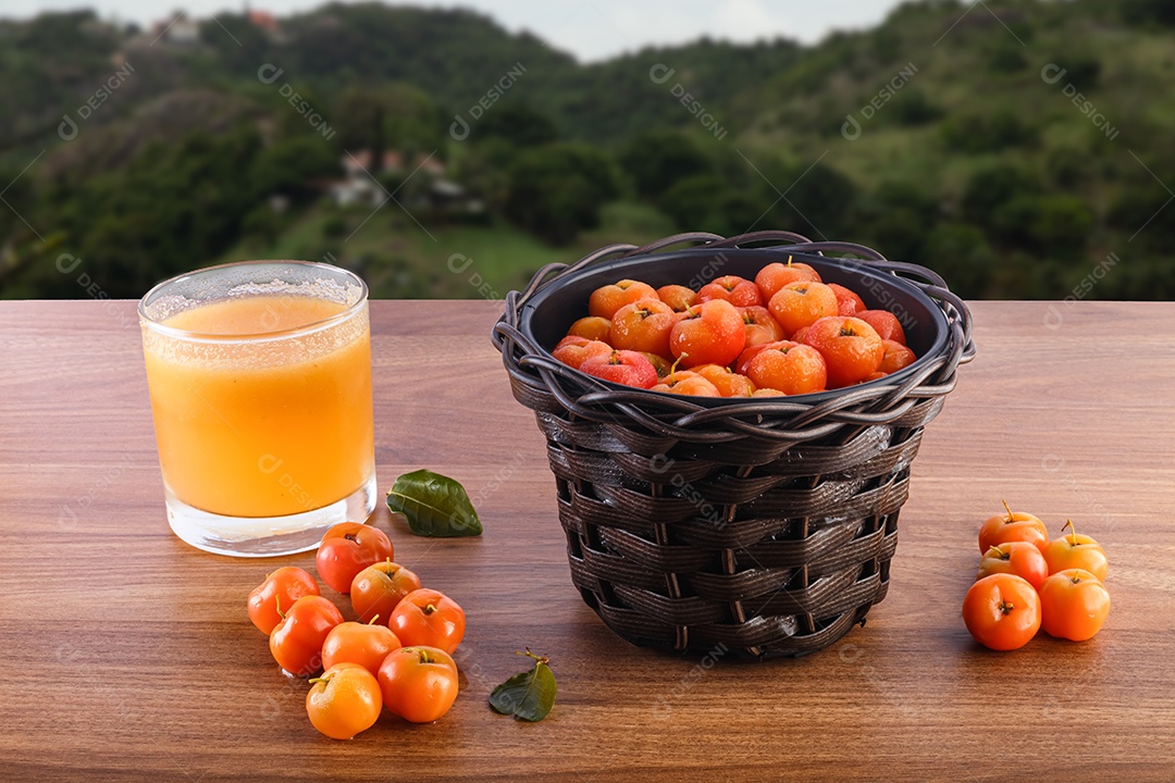 Suco de acerola e acerolas cruas na mesa de madeira na natureza.