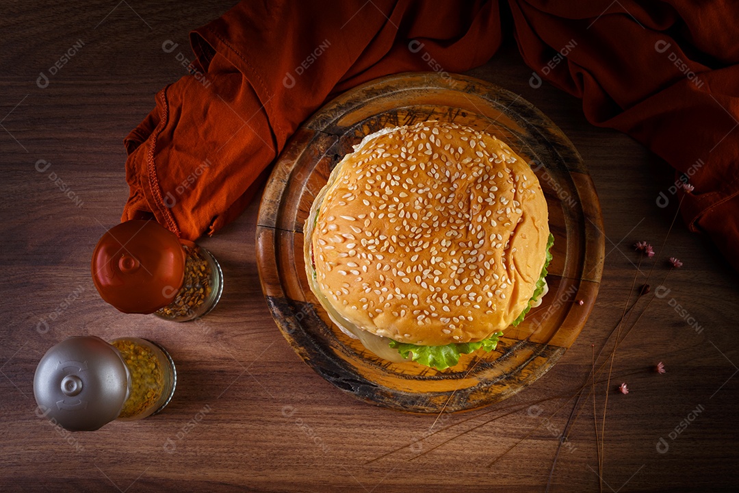 Delicioso hambúrguer na mesa de madeira, especiarias e tecido marrom.