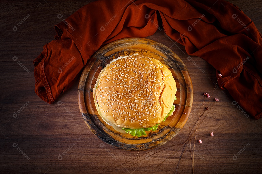 Delicioso hambúrguer na mesa de madeira, especiarias e tecido marrom.