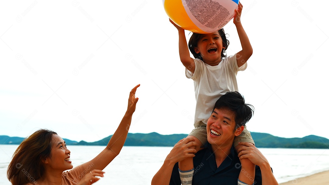 A família feliz do pai carregando o filho brinca com a bola lá fora na praia juntos se divertindo