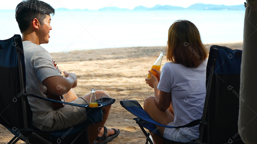 Casal asiático curtindo juntos acampar na praia macho tocando ukulele se divertindo