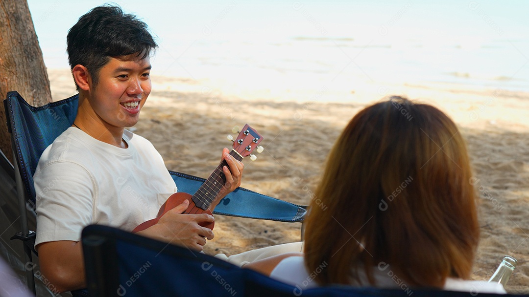 Casal asiático curtindo juntos acampar na praia homem tocando ukulele