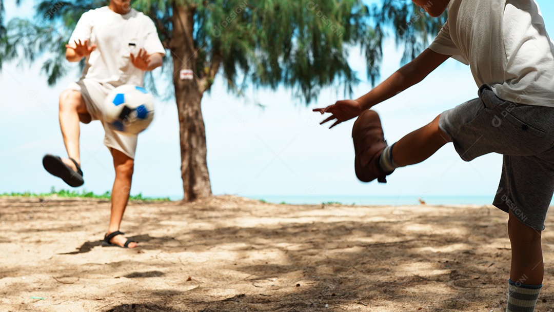 Pai e filho jogando futebol na praia de verão