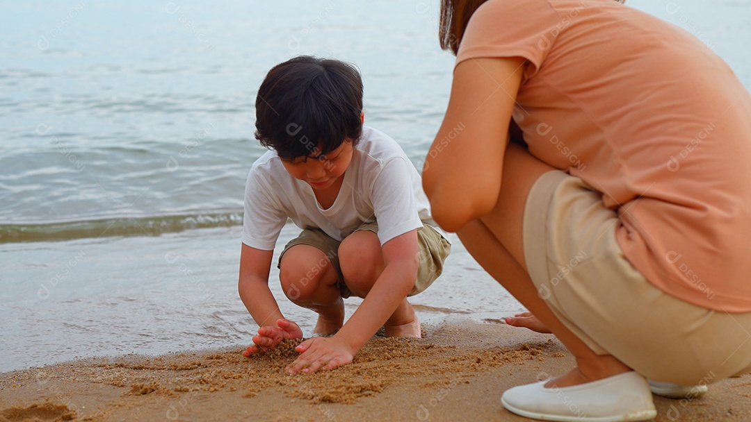 Mãe e filho asiático jogando areia na praia juntos se divertindo
