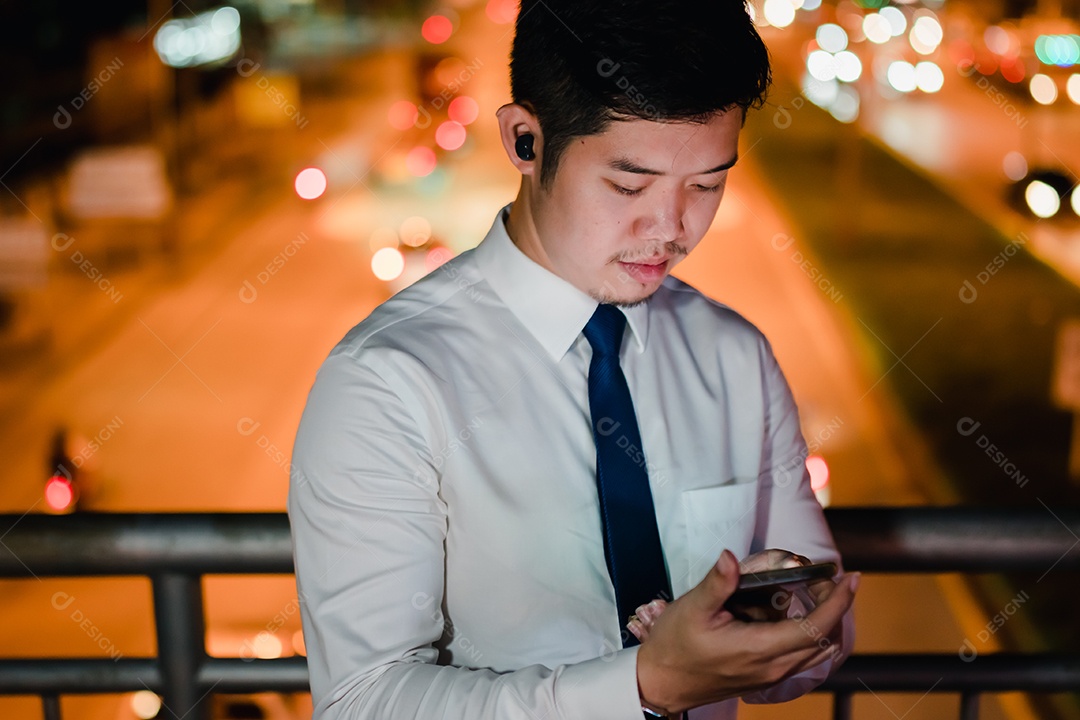 Empresário asiático usa fones de ouvido sem fio ouvindo música na cidade moderna à noite