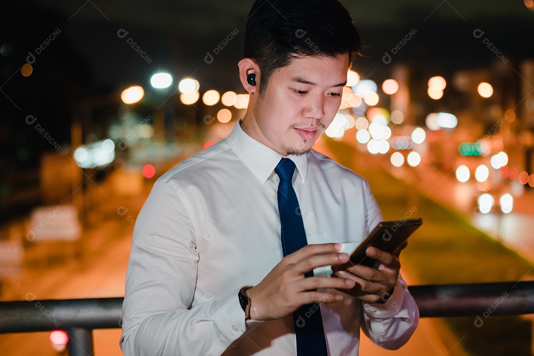 Empresário asiático usa fones de ouvido sem fio ouvindo música na cidade moderna à noite