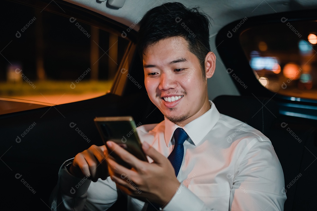 Empresário asiático com telefone inteligente bem-sucedido trabalhando tarde da noite sentado no banco de trás