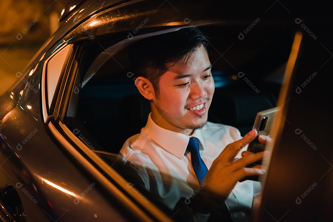 Empresário asiático com telefone inteligente bem-sucedido trabalhando tarde da noite sentado no banco de trás