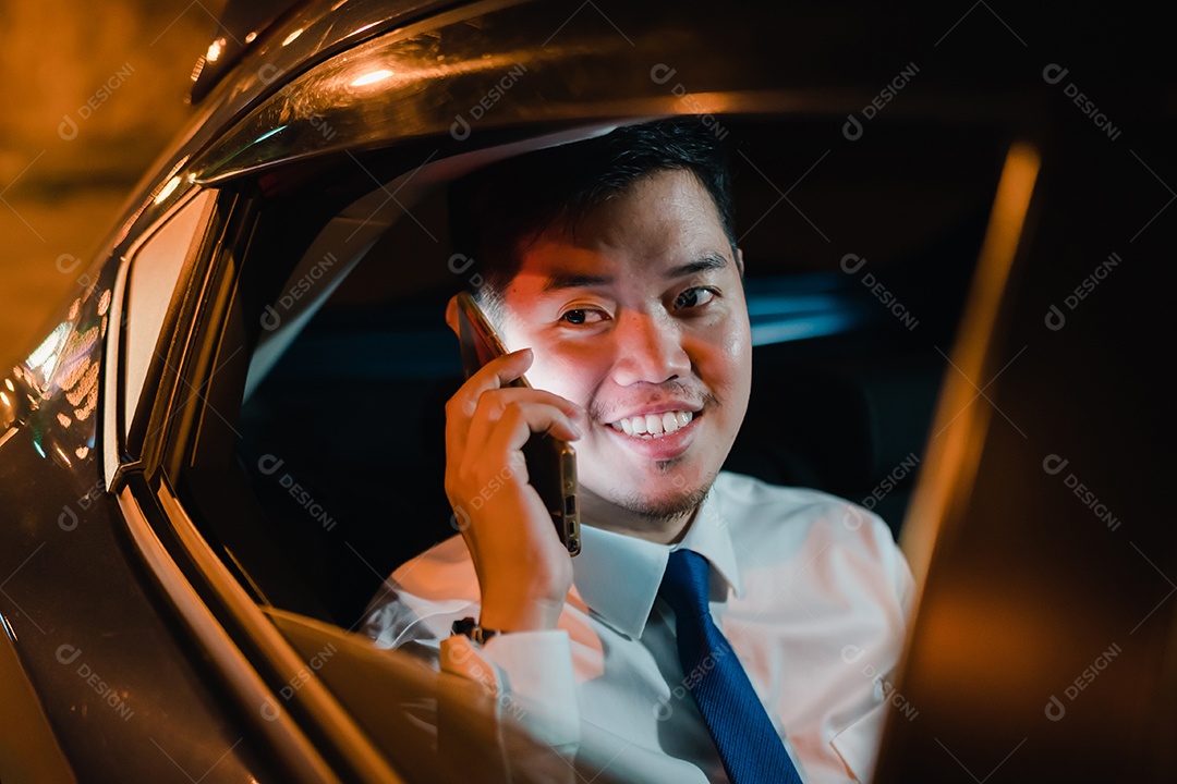 Empresário asiático com telefone inteligente bem-sucedido trabalhando tarde da noite sentado no banco de trás