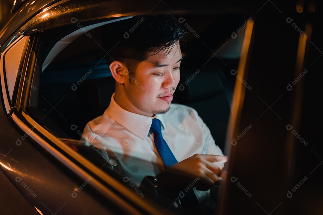 Empresário asiático com telefone inteligente bem-sucedido trabalhando tarde da noite sentado no banco de trás