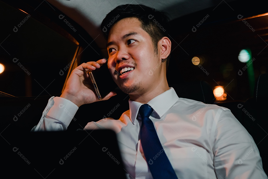 Empresário asiático com telefone inteligente bem-sucedido trabalhando tarde da noite sentado no banco de trás