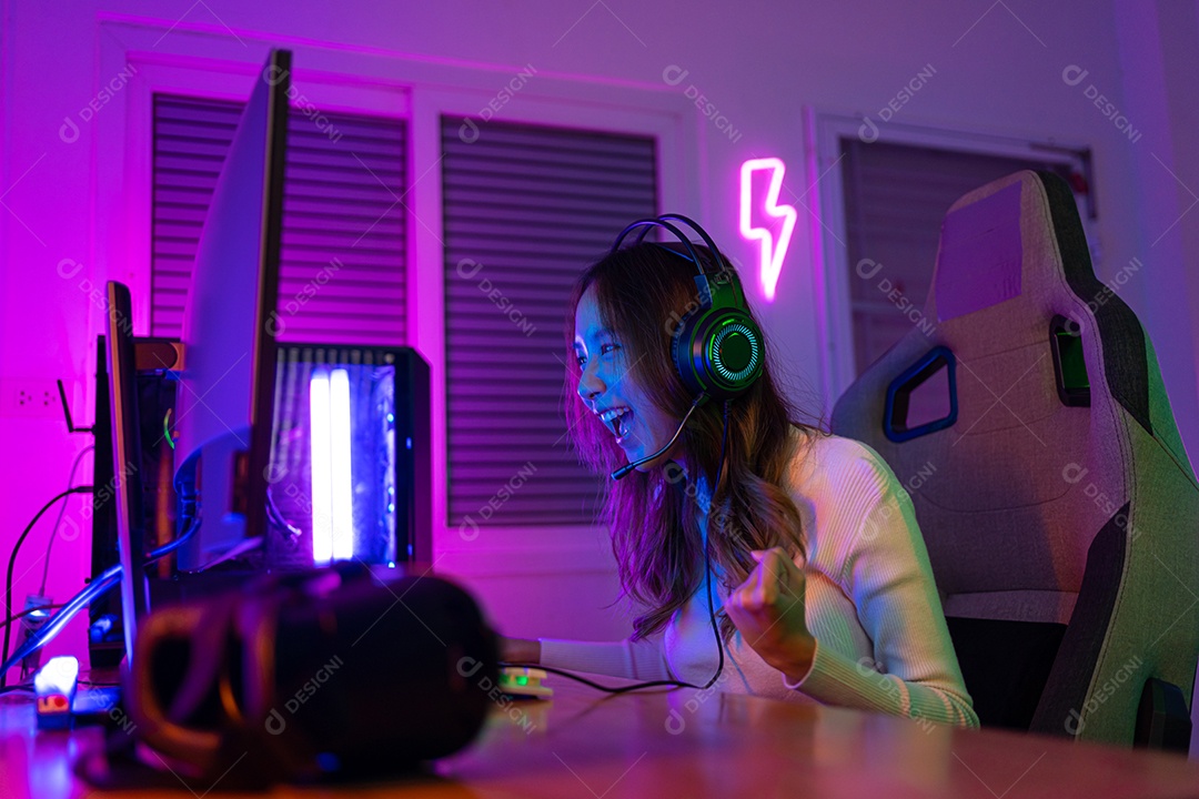 Jogador asiático jogando videogame online ganhando entusiasmo no PC com efeito de iluminação