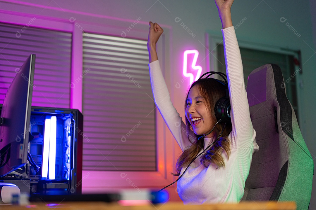 Jogador asiático jogando videogame online ganhando entusiasmo no PC com efeito de iluminação