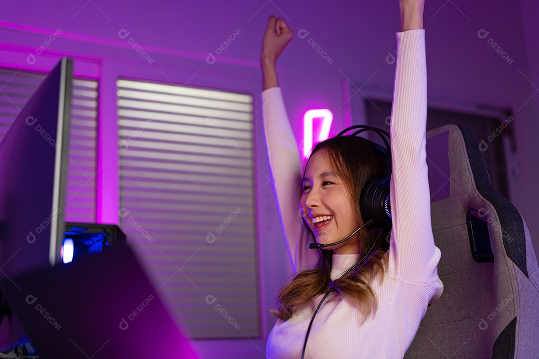 Jogador asiático jogando videogame online ganhando entusiasmo no PC com efeito de iluminação, transmissão ao vivo em casa.