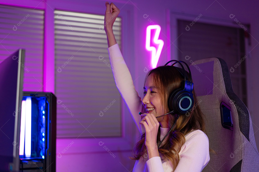 Jogador asiático jogando videogame online ganhando entusiasmo no PC com efeito de iluminação, transmissão ao vivo em casa.