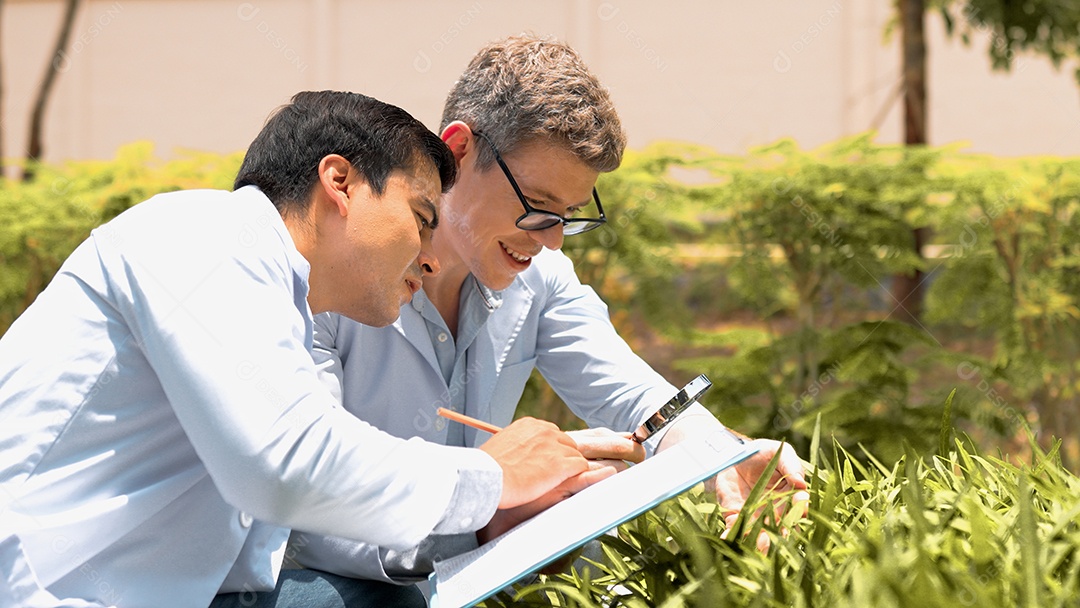 Dois jovens biotecnólogos de jaleco branco usam lupa para verificar plantas