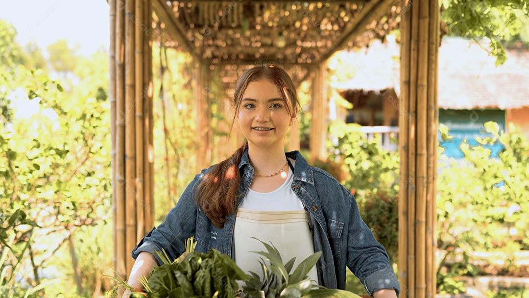 Mulher jovem feliz segurando caixote de madeira com legumes orgânicos frescos da fazenda