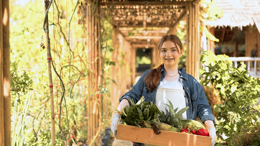 Mulher jovem feliz segurando caixote de madeira com legumes orgânicos frescos da fazenda