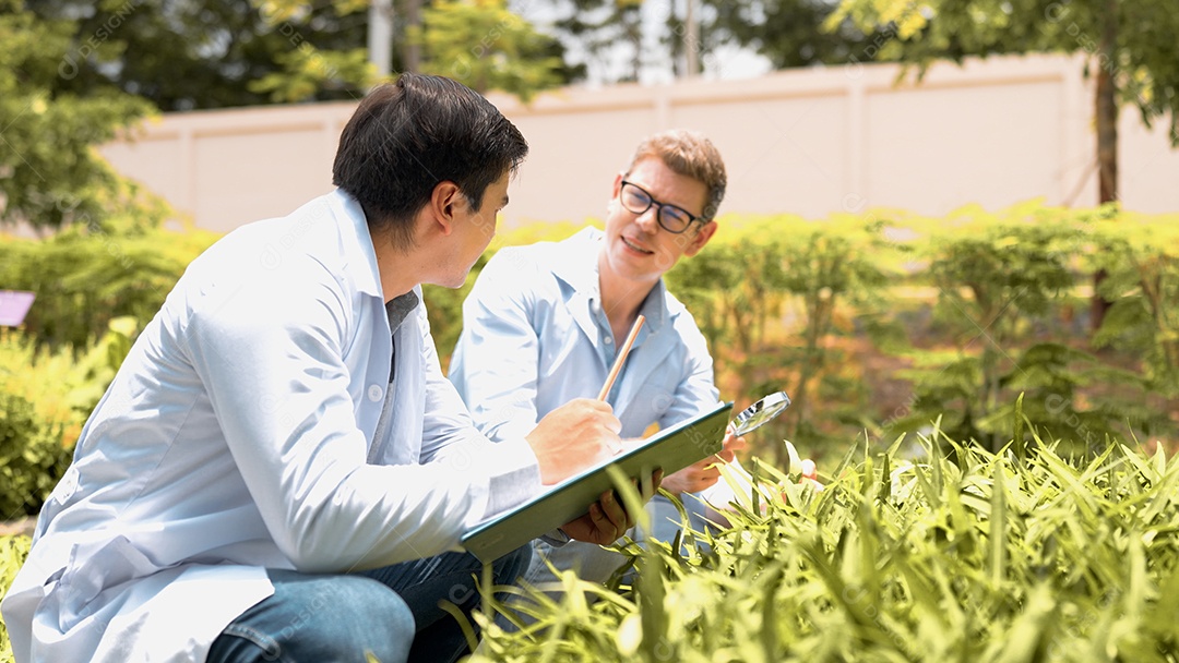 Dois jovens biotecnólogos de jaleco branco usam lupa para verificar