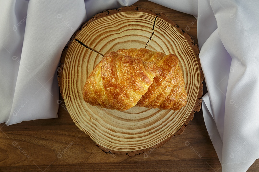 Deliciosos croissants em tronco de madeira, com toalha branca ao redor.