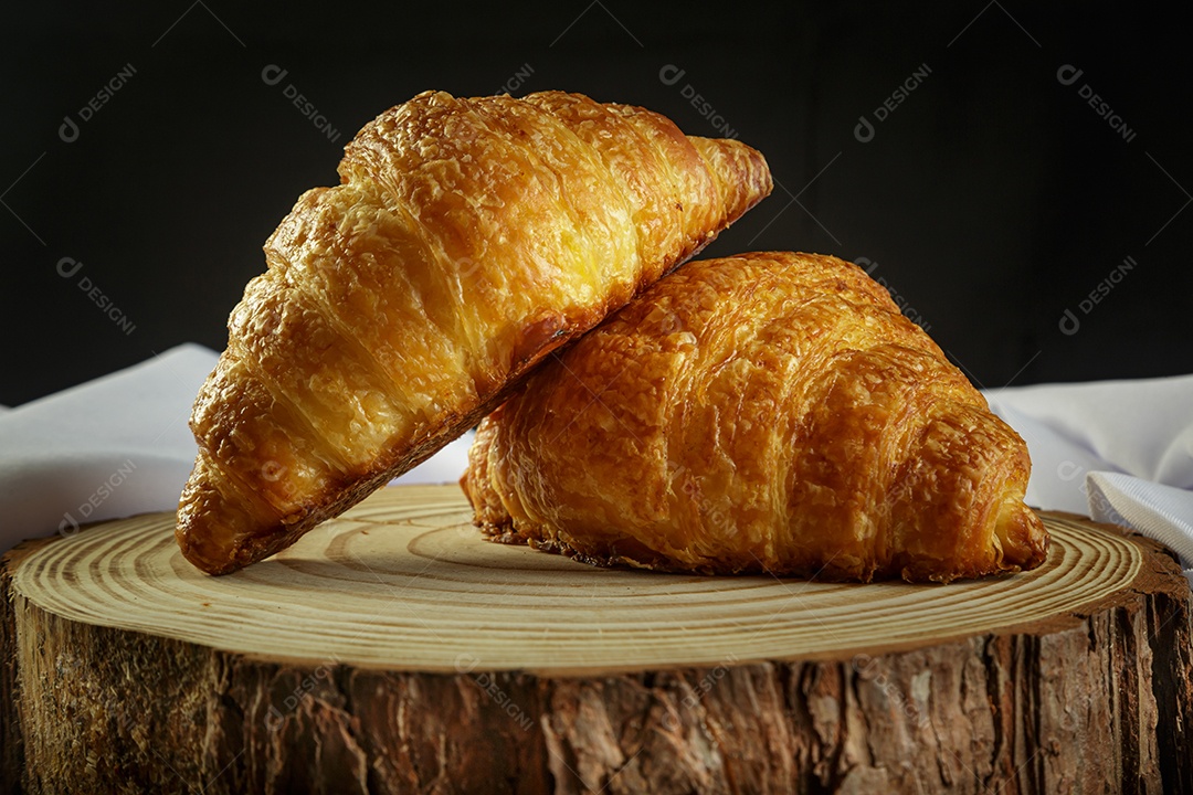 Deliciosos croissants em tronco de madeira, com toalha branca ao redor.