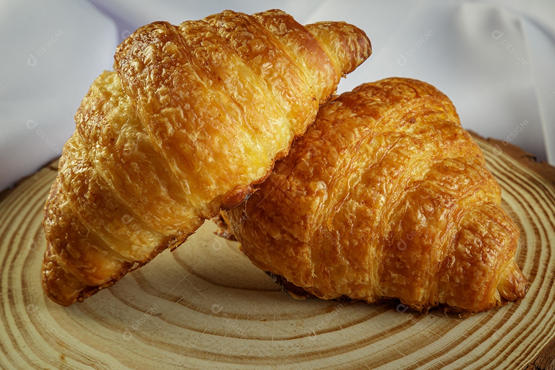 Deliciosos croissants em tronco de madeira, com toalha branca ao redor.